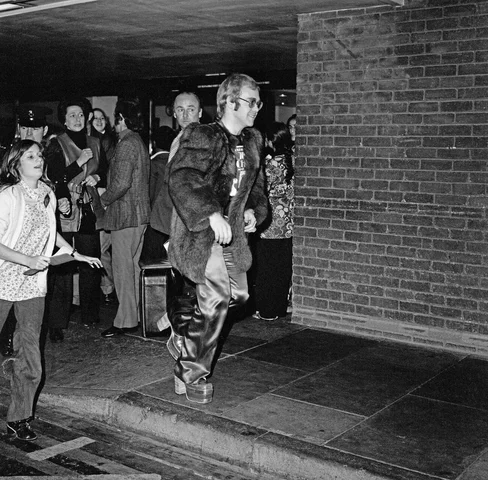 Elton John arrives at Heathrow Airport, and has to run from the crowds of fans who are waiting there. It is not clear if Elton is flying in, or flying out. Picture taken 29th October 1972