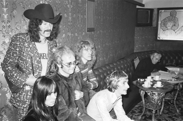 Elton John and his group pose for pictures in the Palladium bar during rehearsals for the Royal Variety Show. Musical director Burt Rhodes can be seen writing out the orchestra parts. 29th October 1972