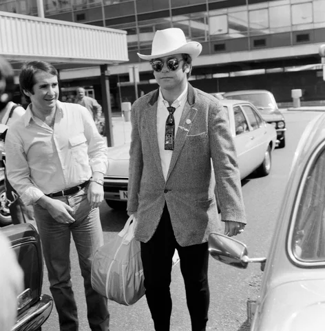 Dressed in a stetson hat, Elton John leaves Heathrow Airport for America. On the left is John Reid, Elton's manager. 10th August 1980.