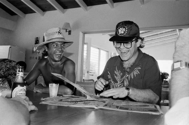 Elton John And Bernie Taupin Elton John (right) and lyricist Bernie Taupin on the Caribbean island of Montserrat, 11th October 1982. Elton is on the island to record his new album, 'Too Low for Zero', at AIR studios.
