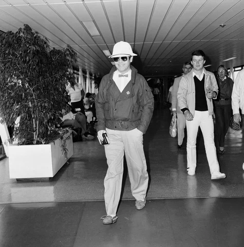Elton John leaving Heathrow Airport for Paris to make a TV appearance. 29th June 1983.
