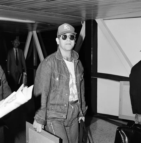 Singer Elton John, arrives at Heathrow airport from Australia, where he has been watching cricket. 7th February 1983.