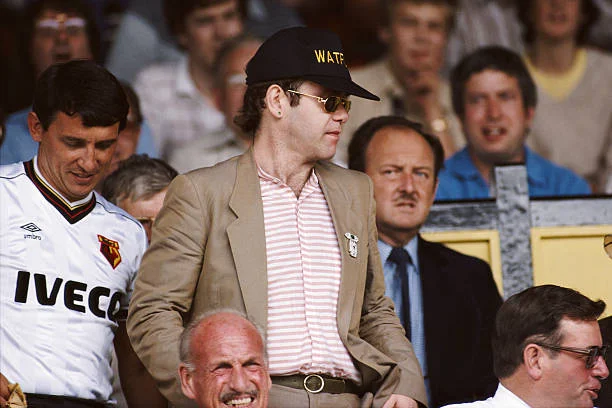 WATFORD, UNITED KINGDOM - AUGUST 19: Watford chairman Elton John (c) and manager Graham Taylor (l) take their seats prior to a match at Vicarage Road, circa 1984 in Watford, England.