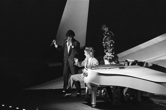 Elton John in concert during his Ice on Fire Tour, pictured performing at Wembley Arena. Elton, wearing a towering crown, is joined on stage by George Michael and Rod Stewart. 19th December 1985.