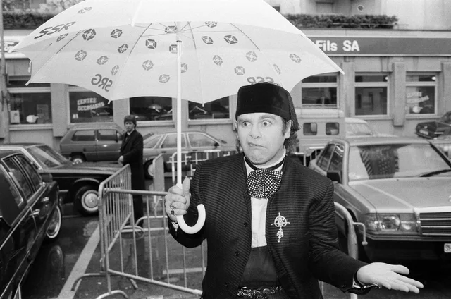 Elton John standing in the rain. He is in Montreux to perform at the Montreux Pop Festival. 9th May 1985.