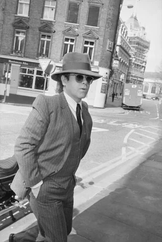 British singer-songwriter Elton John wearing a three-piece pinstripe suit with a fedora and sunglasses, United Kingdom, 12th March 1985.