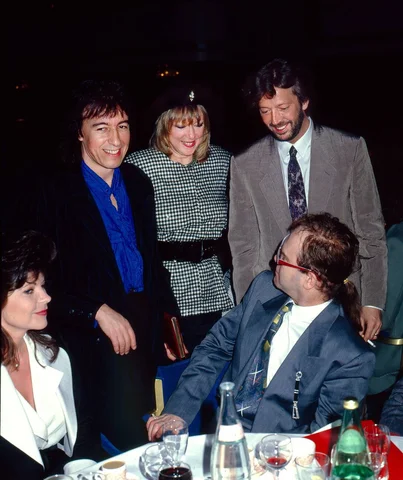 Eric Clapton at the Ivor Novello Awards on May 7, 1986, with Pattie Boyd and Bill Wyman, saying hello to Elton John and his ex-wife Renate Blauel.