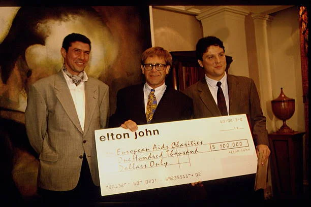 British singer and songwriter Sir Elton John gives a cheque to the anti-AIDS fight